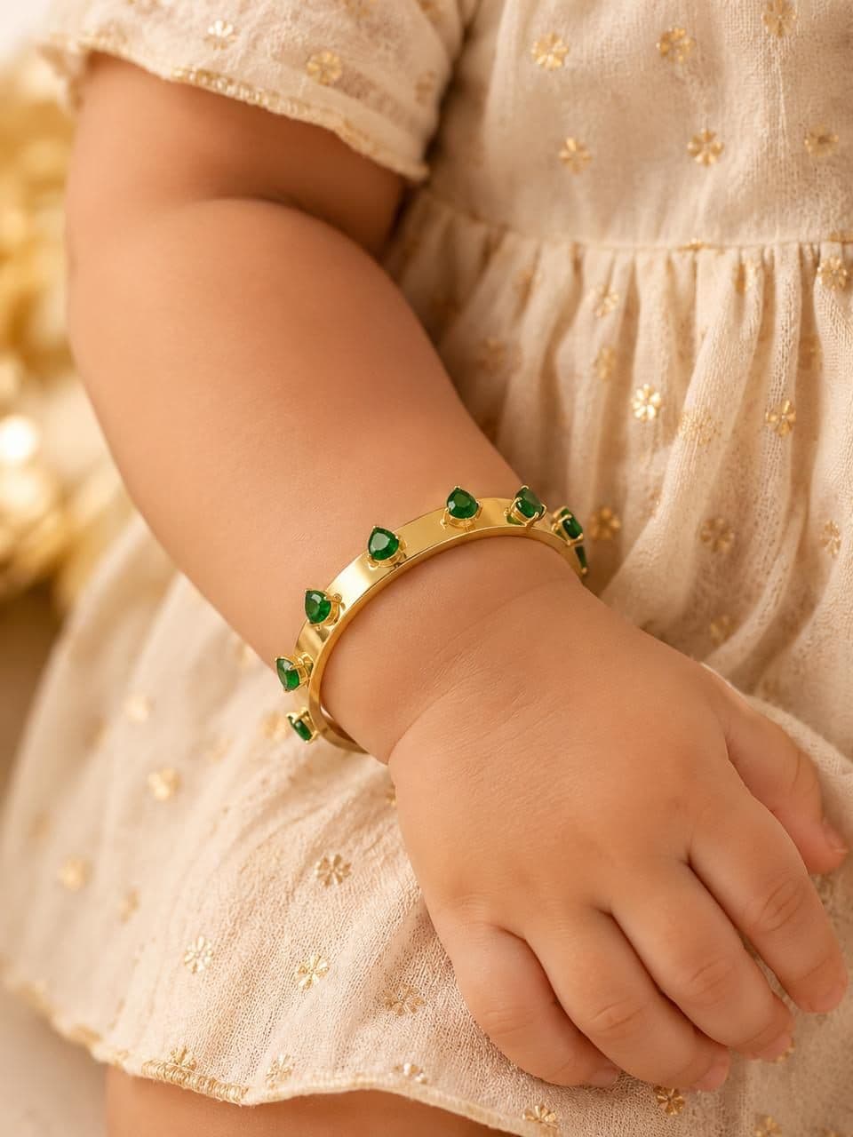 Child wearing a gold bangle with green stones